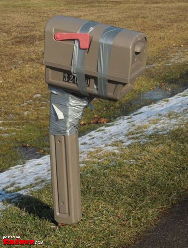 A mailbox sitting in the snow with tape on it, surrounded by a serene winter scene.