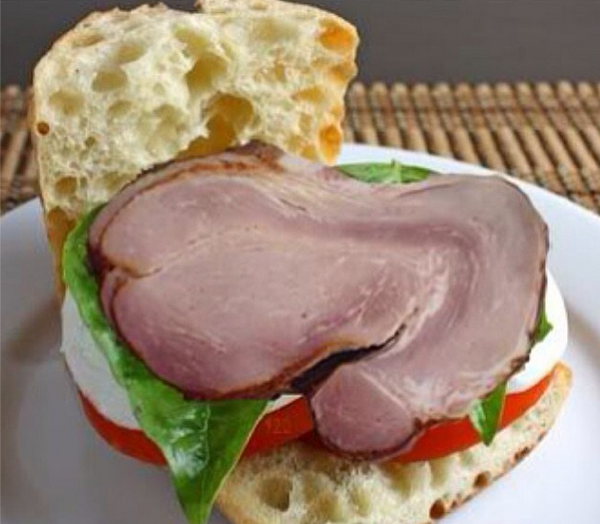 A smile-inducing sandwich with ham and tomatoes on a white plate.