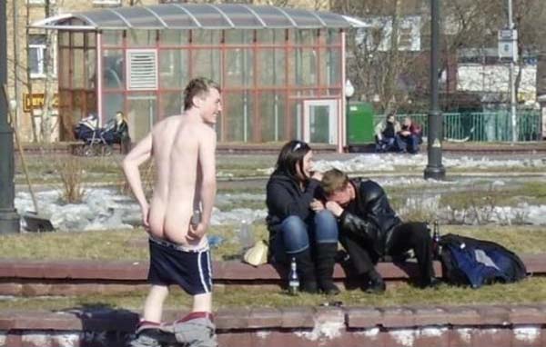 A naked man is sitting on a bench in a park.