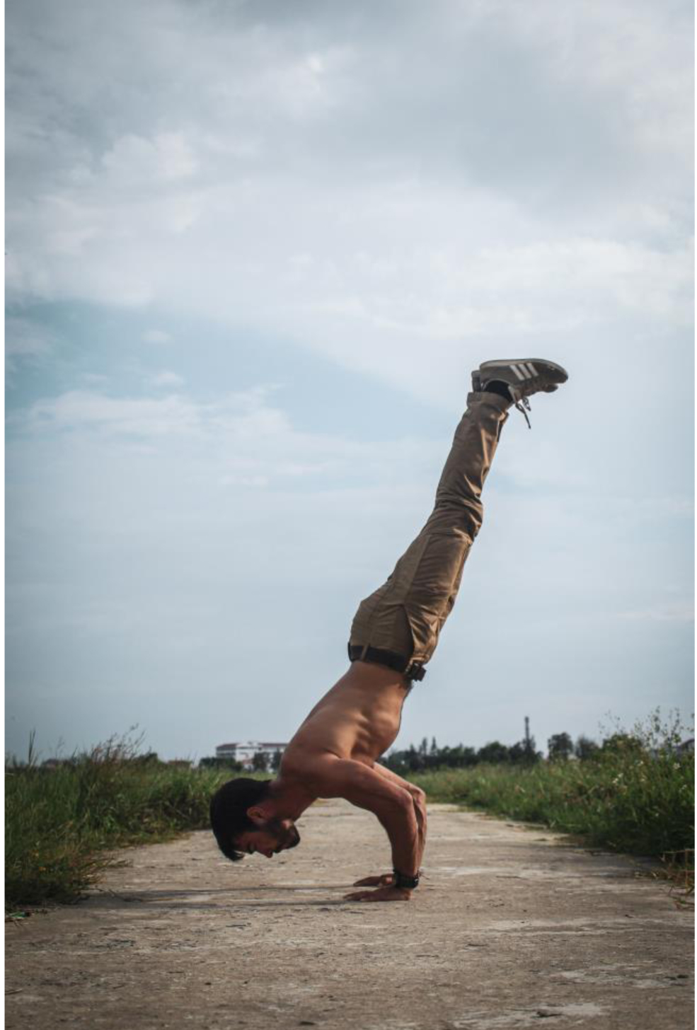 A man demonstrating calisthenics with a handstand on a road.