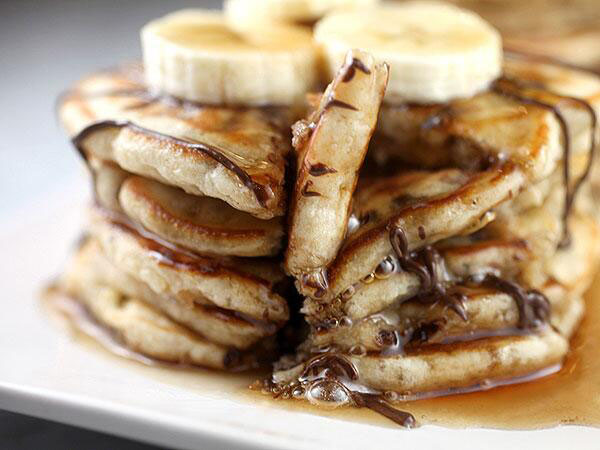 A stack of decadent pancakes topped with chocolate syrup and banana slices that will leave you craving for more - food porn alert!