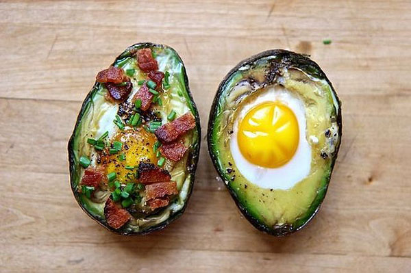 Warning: Food Porn Ahead - Two avocados with eggs and bacon on a wooden table, tantalizingly plated.