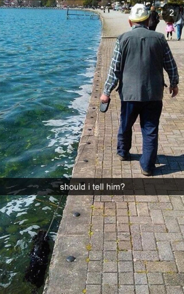 An old man captures funny Snapchats while walking his dog near the water.