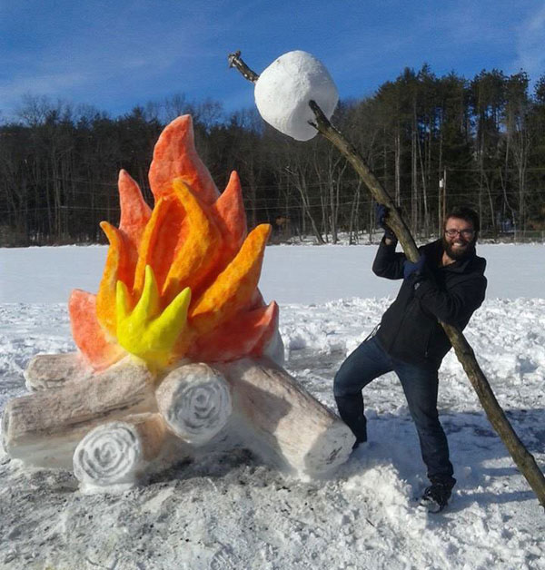 A man standing next to a snow sculpture and fire embracing The Snow Art.