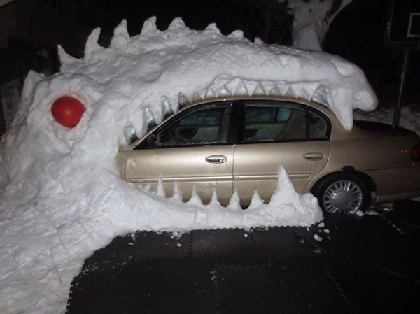 A snow-covered car adorned with a monstrous head provides an artistic relief during winter.