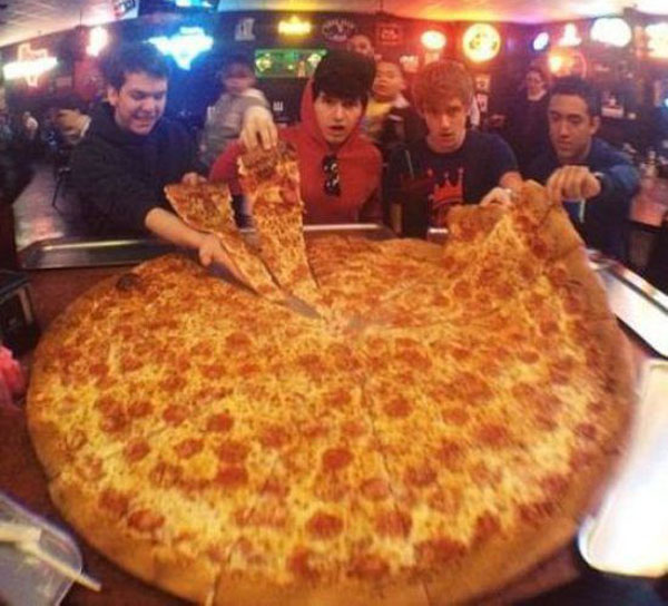 A group of people standing around a large pizza, tempted to indulge in their wants rather than their needs.