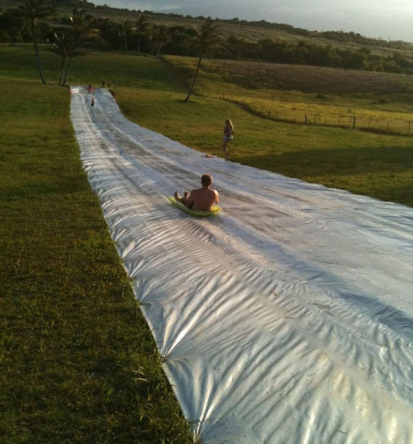 A group of people enjoying a thrilling water slide adventure in a grassy field.