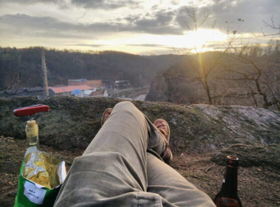 A person indulging in weekend confessions, sitting on a rock with a bottle of wine and a bottle of beer.