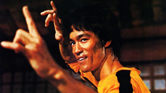 Bruce Lee, the legendary martial artist, wearing a yellow shirt and striking a powerful hand gesture.
