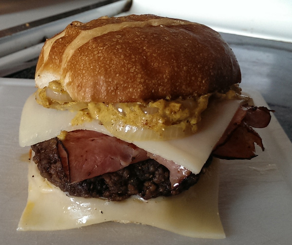 A food porn-worthy burger with ham and cheese presented on a white plate.
