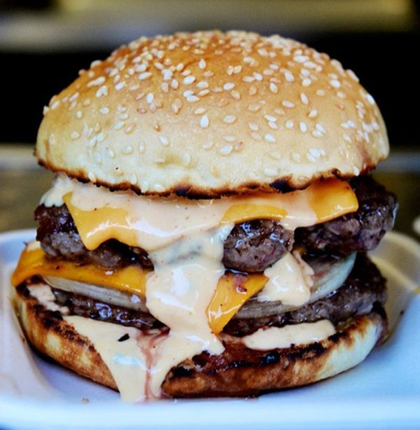 A cheesy burger served on a plate, perfect for food porn enthusiasts.