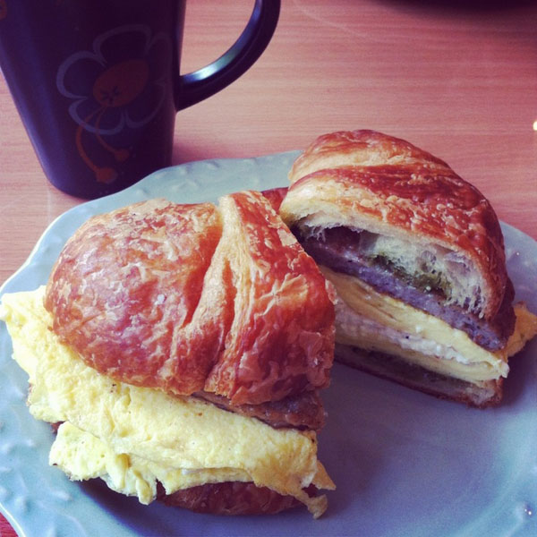 A drool-worthy croissant sandwich and coffee on a plate.