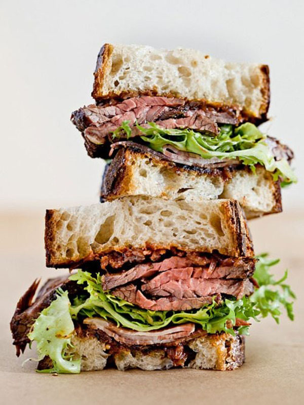 A mouthwatering sandwich, featuring steak and lettuce, beautifully presented on a paper.