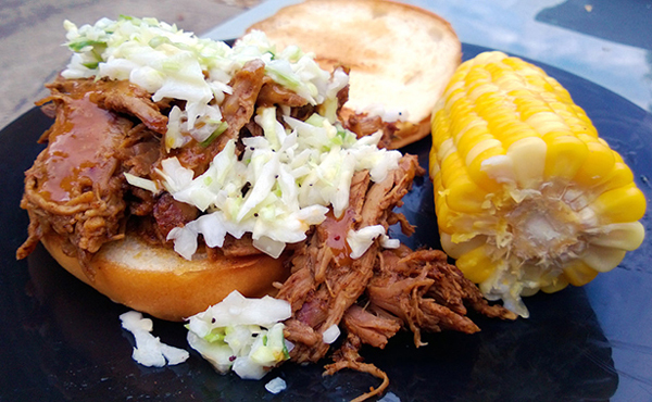 A mouthwatering pulled pork sandwich, topped with coleslaw and served with corn on the cob.