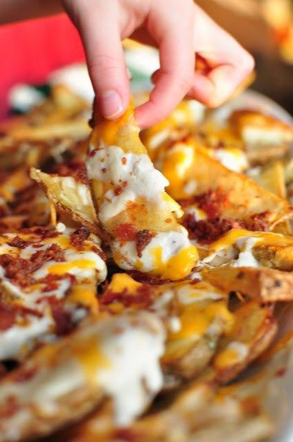 A person enjoying Game Day Grub Ideas by grabbing a plate of nachos with cheese and bacon.