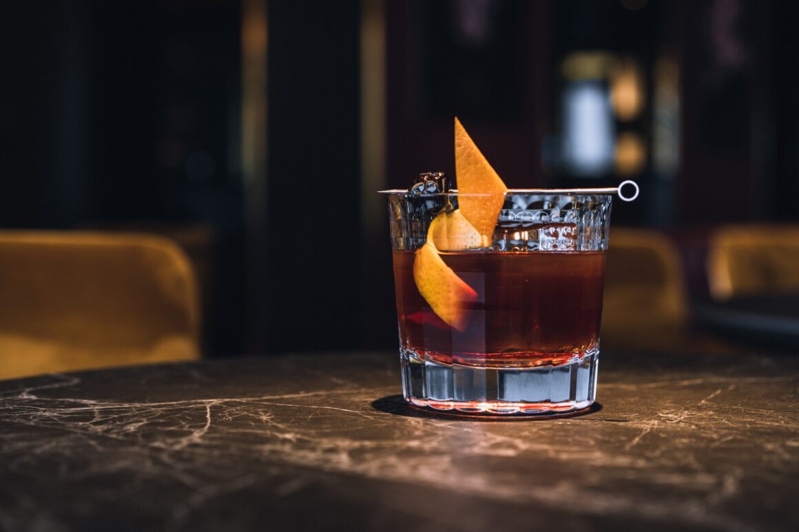 A cocktail garnished with an orange that initiates bar conversations.