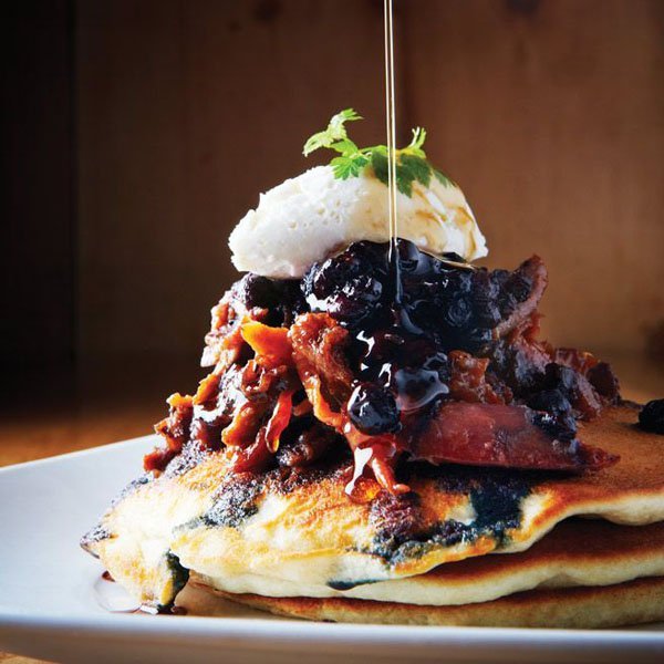 A stack of pancakes topped with blueberry syrup and whipped cream that is OM-F@cking-G It's Food Porn.