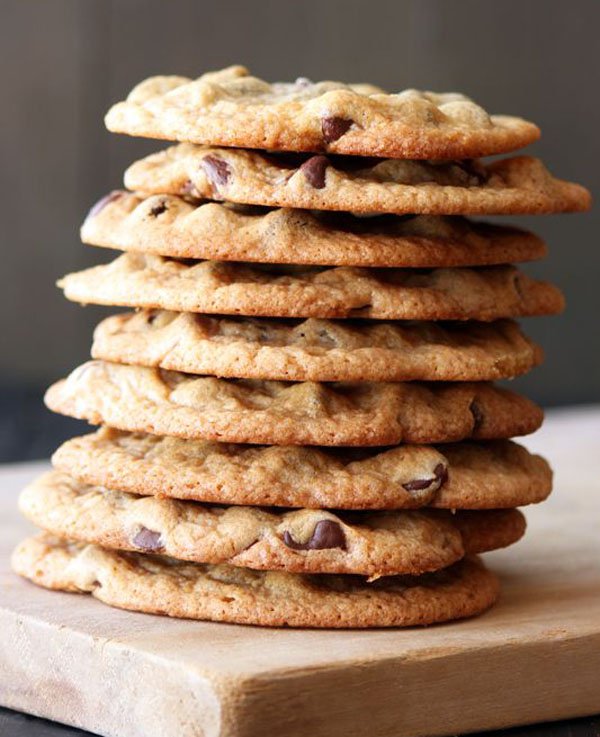 A mouthwatering stack of chocolate chip cookies on a cutting board.