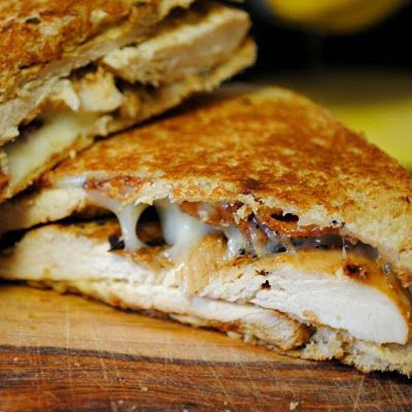 A mouthwatering grilled chicken sandwich on a cutting board.