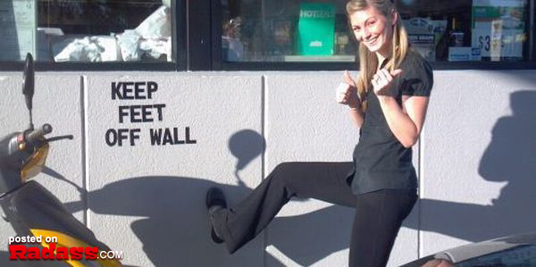 A rebellious woman posing in front of a wall with a "keep feet off wall" sign captures the spirit of the next generation.