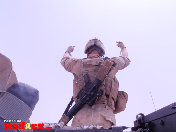 A soldier standing on a vehicle, raising arms in salute.