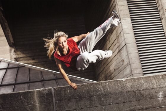 A woman demonstrating parkour skills with an impressive stunt on a concrete wall.