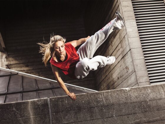 A woman demonstrating parkour skills with an impressive stunt on a concrete wall.