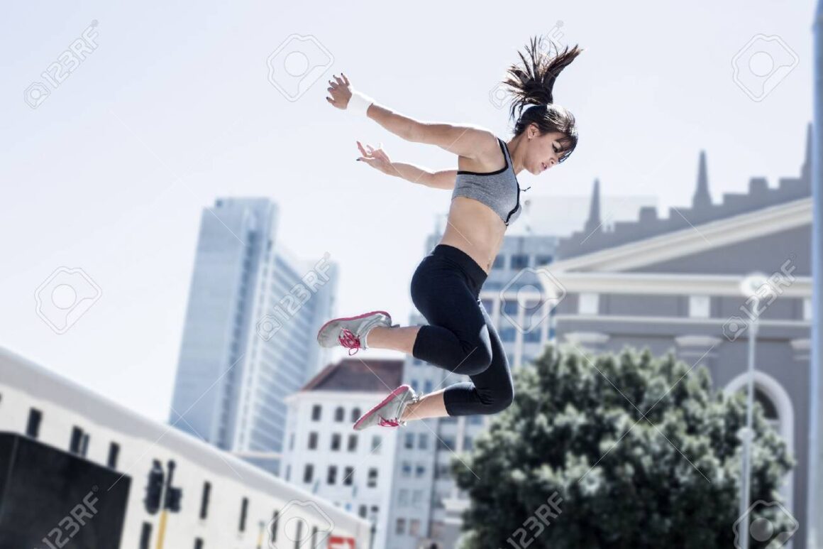 A young woman demonstrating parkour techniques in front of a city stock photo.