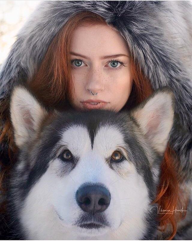 A woman is posing with a husky dog.