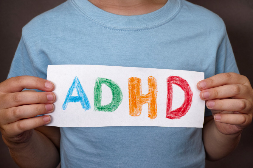 A boy discussing ADHD by holding up a piece of paper with the word adhd on it.