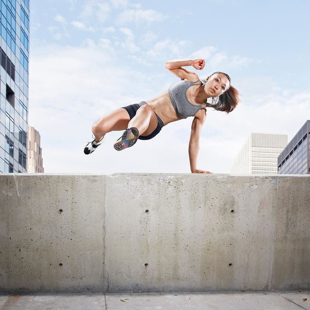 A woman demonstrating parkour by jumping on a concrete wall.