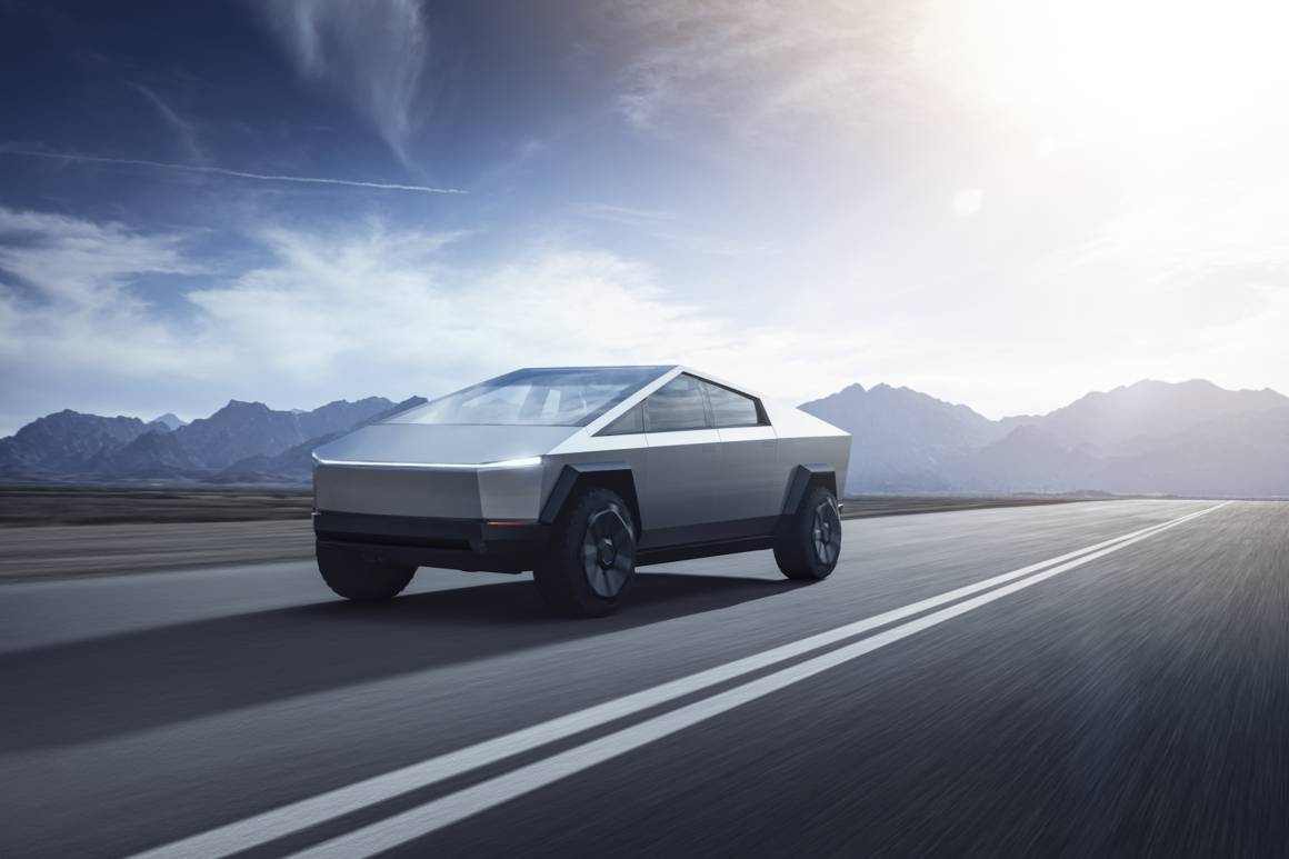 The Cybertruck IS coming, driving down a road with mountains in the background.