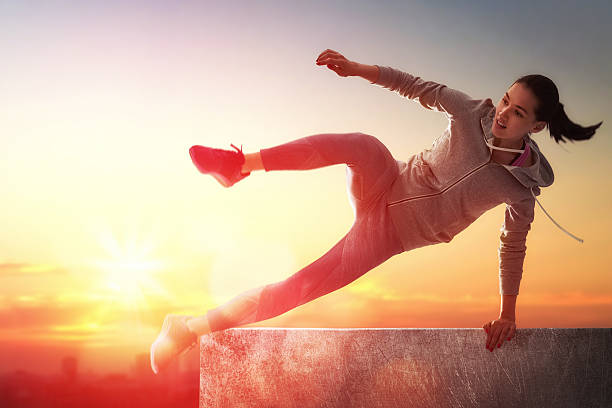 A woman demonstrating parkour with a jump on a wall at sunset.