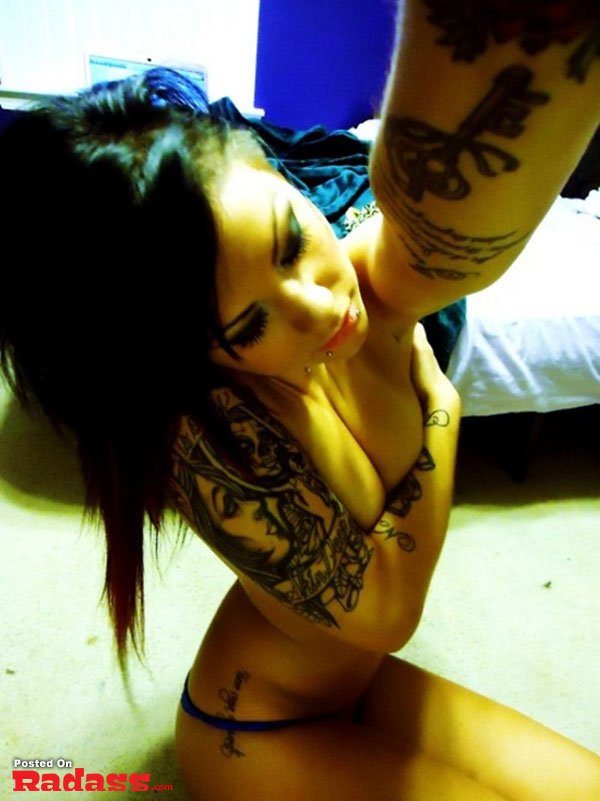 A hot girl with tattoos flaunting her ink while posing seductively on a bed.