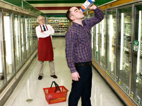 A man standing in a grocery store holding a bottle of water, proving that the customer is not always right.