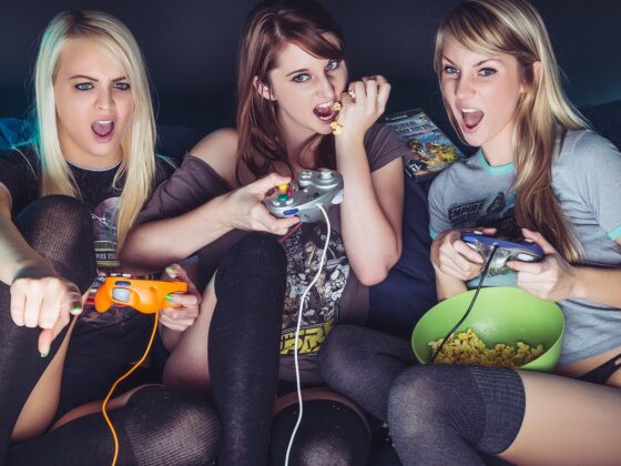 Three girls sitting on a couch with video game controllers.